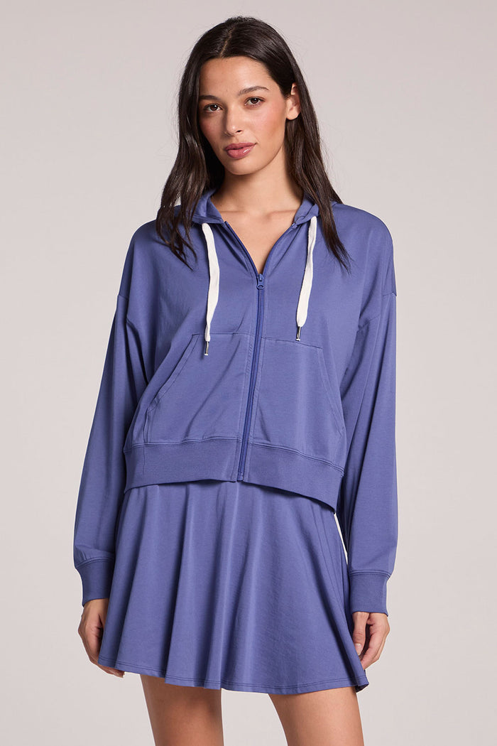 Front of a woman wearing the Chaser French Riviera Abilena Zip-Up on a neutral background, with one hip cocked