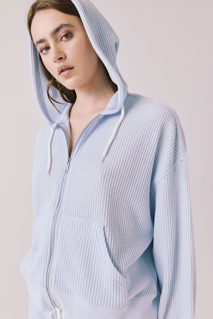 Side view of woman wearing the Abilene Light Skyway Blue Zip Up Hoodie with the hoodie up on a white background