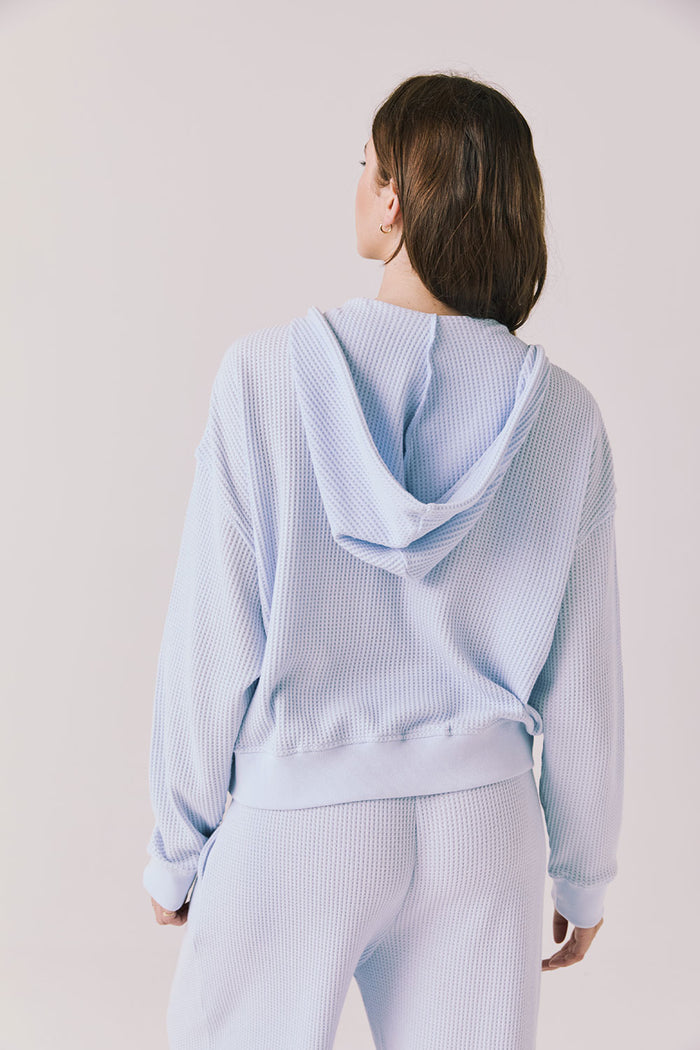 Back view of woman wearing the Abilene Light Skyway Blue Zip Up Hoodie with matching pants on a white background