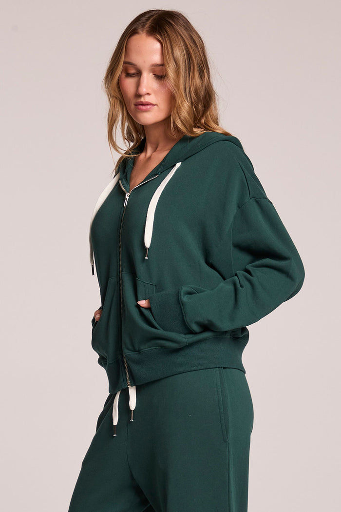 Side view of a woman wearing the Chaser  Abilene Pine Pullover on a neutral background with hands in pockets