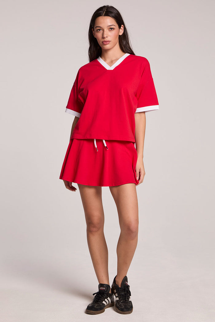 A full body front view of a woman wearing the Chaser Cardinal Red Ace Mini Skort and matching Eden Tee on a neutral background