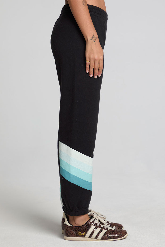 Side view of a woman wearing the Chaser Ada Black Jogger on a neutral background with arms at sides and sneakers