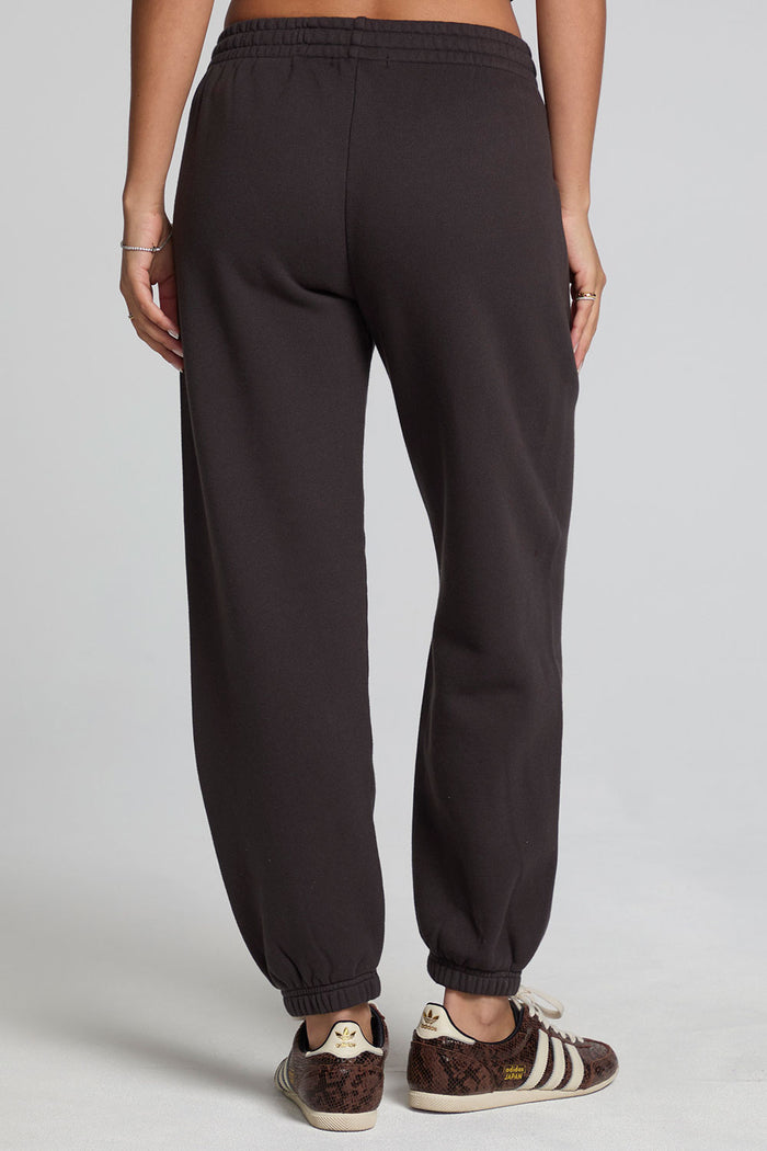Back view of a woman wearing the Chaser Ada Dark Heather Grey Jogger on a neutral background with brown striped sneakers