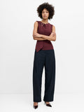 A model stands against a plain white studio background wearing dark navy wide-leg trousers with pleating detail on the hips.