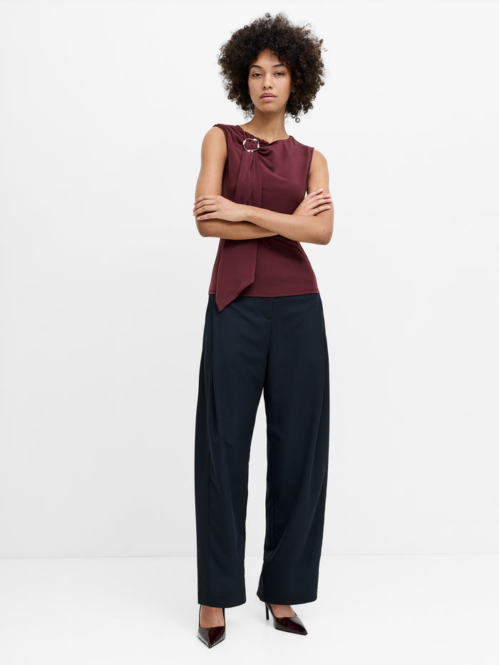 A model stands against a plain white studio background wearing dark navy wide-leg trousers with pleating detail on the hips.
