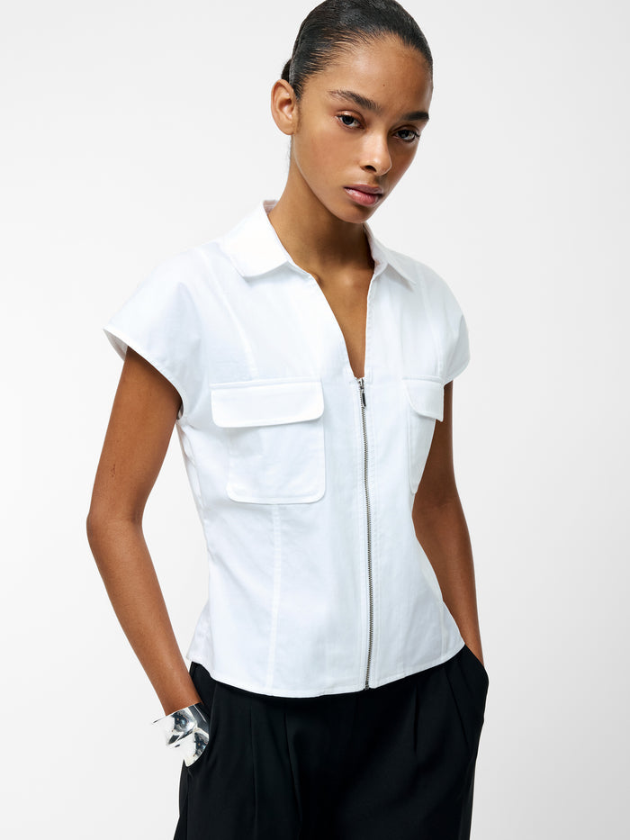 A woman wearing a white v-neck zip through top with 2 front pockets and short sleeves.