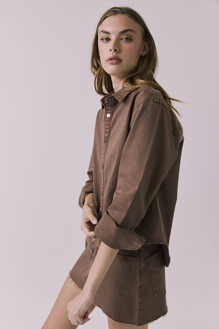 Side view of a woman wearing the Chaser brown All Day Cognac Wash Button Down with matching Sloane Mini Skirt against a plain background