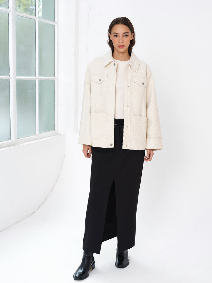 Woman wearing a black skirt and a cream boucle long sleeve overshirt