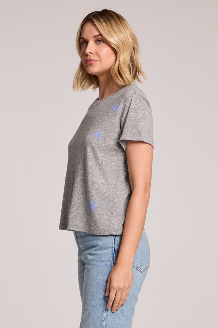 Side view of a woman wearing the Chaser  Allover Stars Tee on a neutral background with her arms at her side