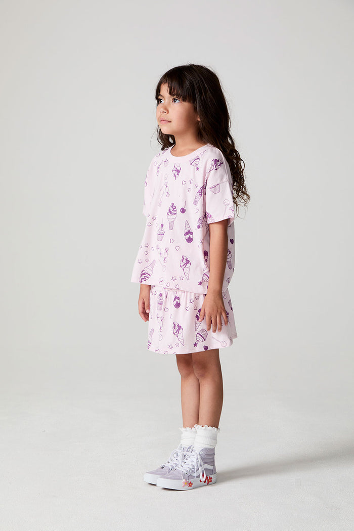 Full body side view of a girl wearing the Chaser Allover Sweets Tee on a neutral background