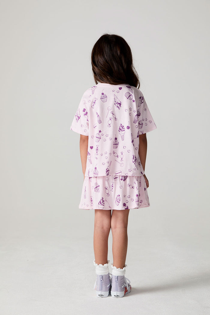 Full body back view of a girl wearing the Chaser Allover Sweets Tee on a neutral background