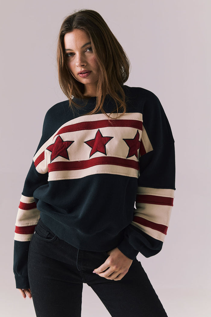 Woman wearing a black sweater with red and white star design on a plain background