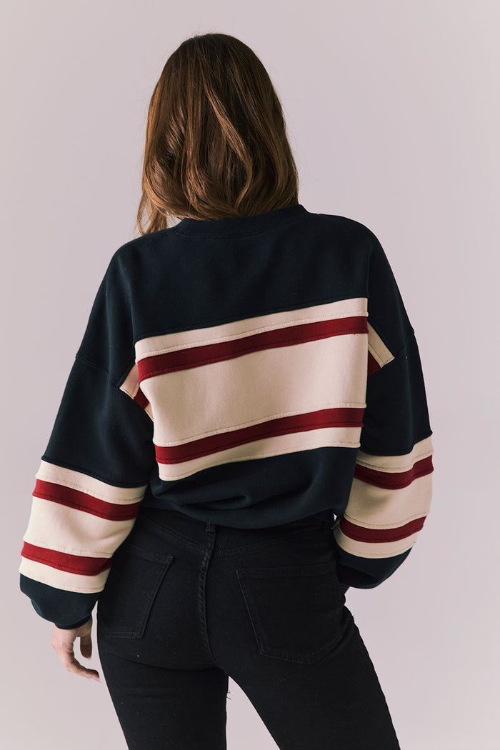 Person wearing a black sweater with red and beige stripes on a plain background