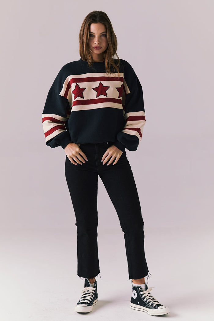 Woman wearing a black sweater with red star patterns and black pants on a light gray background