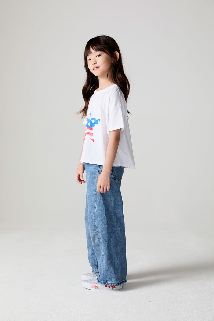 A full body side view of a girl wearing the Chaser  Americana Star Tee on a neutral background