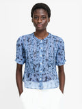 A woman wearing a short sleeved semi sheer floral print ruffle top with front buttons and a round neckline.