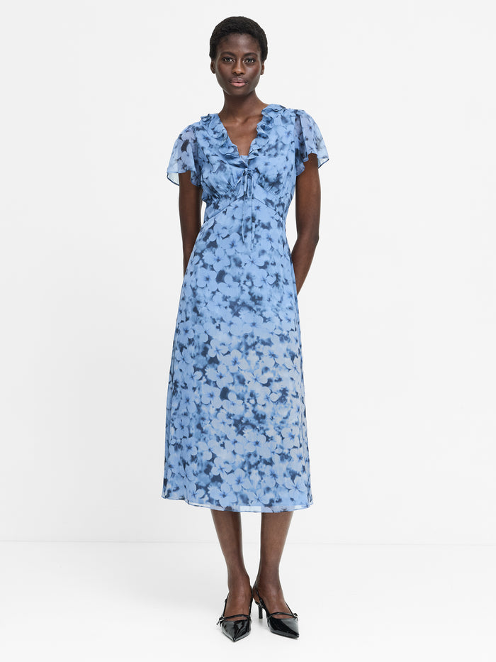 A woman wearing a blue, midi length, short sleeved V-neck dress with a floral pattern.
