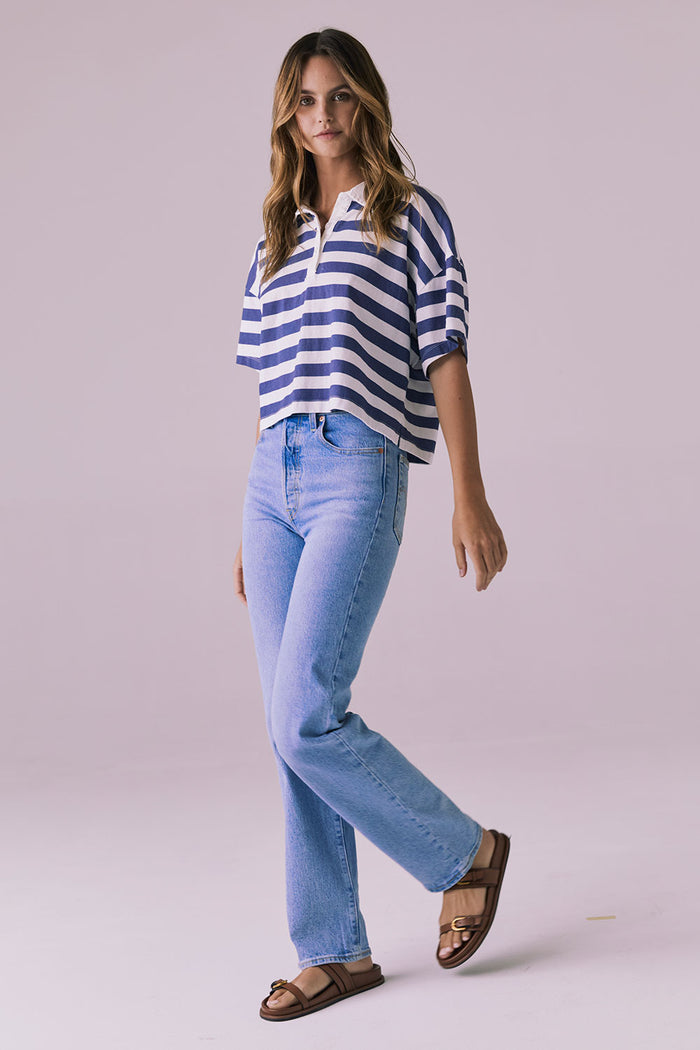 Sideview of a woman wearing the Chaser Antoni Castaway Stripe Tee styled with high-waisted light-wash jeans and sandals in a minimalist studio setting