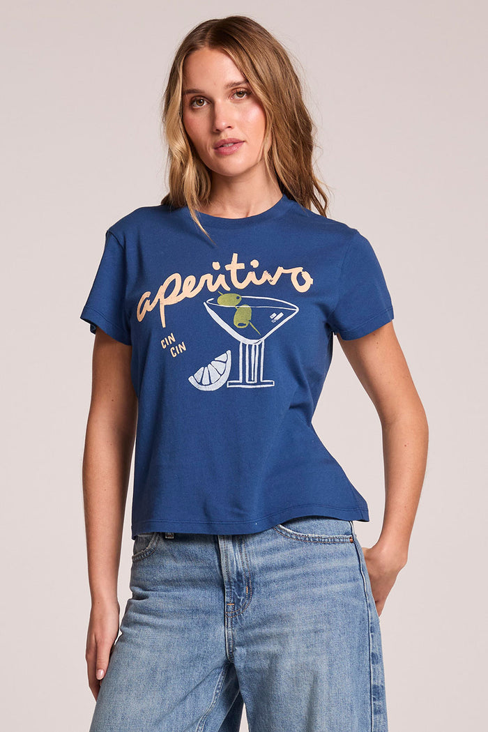 Front view of a woman wearing the Chaser   Aperitivo Tee and jeans on a neutral background with one hand on her hip