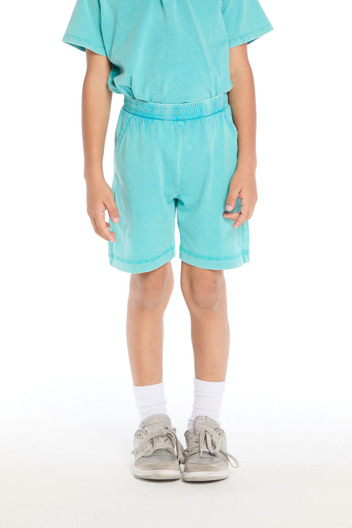 Front view of boy wearing the Chaser Kids Aqua Teal Cozy Beach Shorts with elastic waistband and soft terry texture, paired with the matching Aqua Teal Polo Shirt on a white background