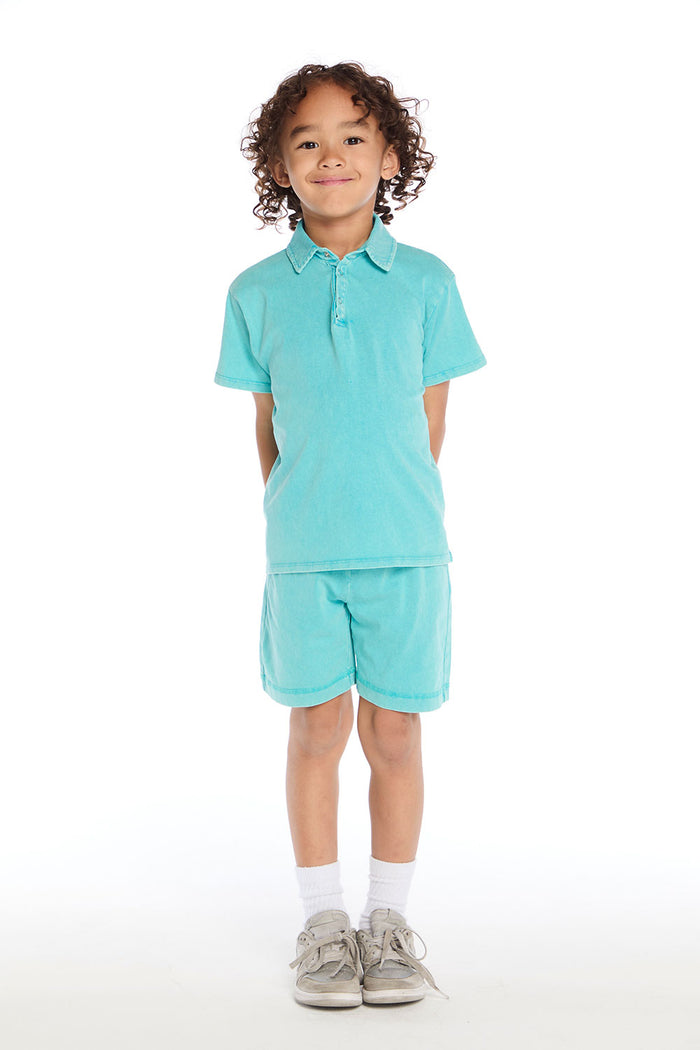 Full body view of boy wearing the Chaser Kids Aqua Teal Cozy Beach Shorts and matching Aqua Teal Polo Shirt styled with white socks and silver sneakers on a white background