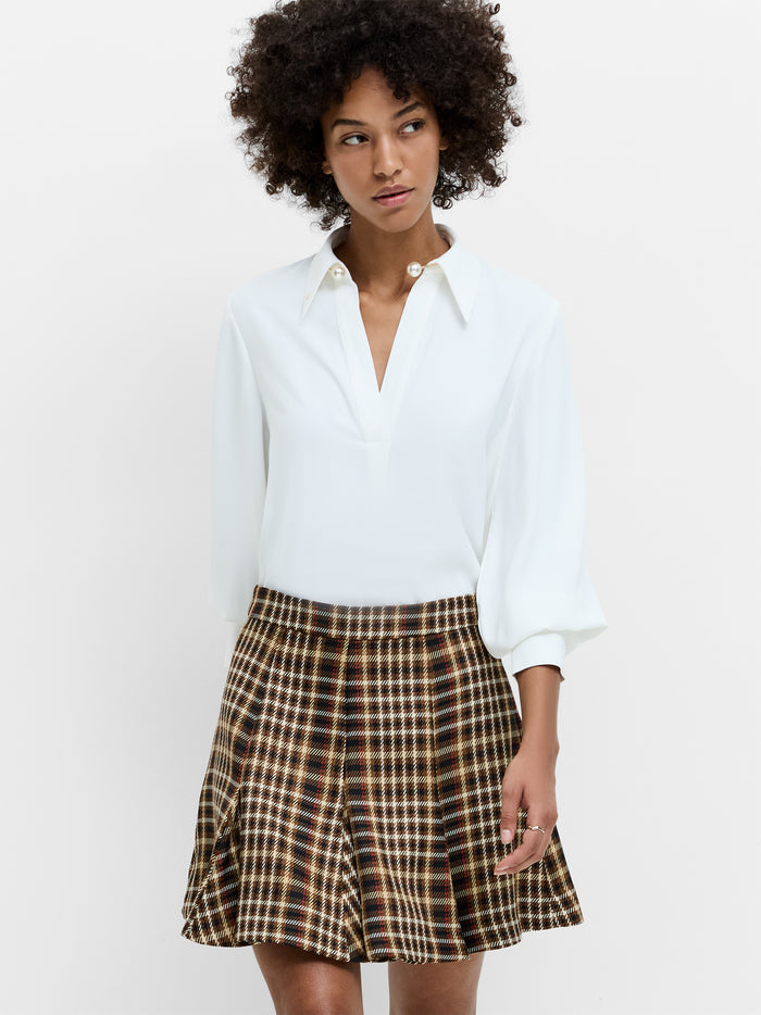 A woman wearing a white pearl trim shirt with balloon sleeves, an oversized pointed collar and a relaxed fit.