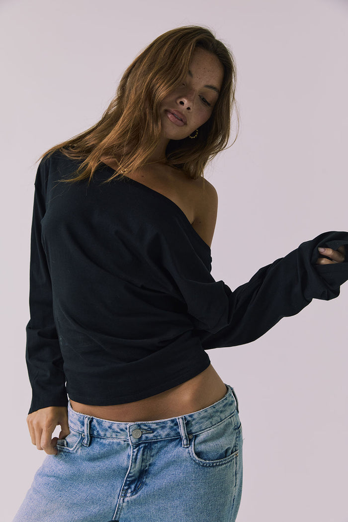 Front view of a woman wearing Chaser off-shoulder Ash Black Long Sleeve and blue jeans against a plain background
