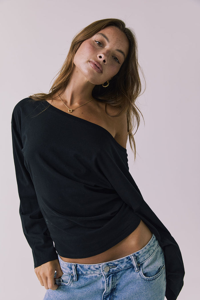 Alternate view of a woman wearing Chaser off-shoulder Ash Black Long Sleeve and blue jeans against a plain background