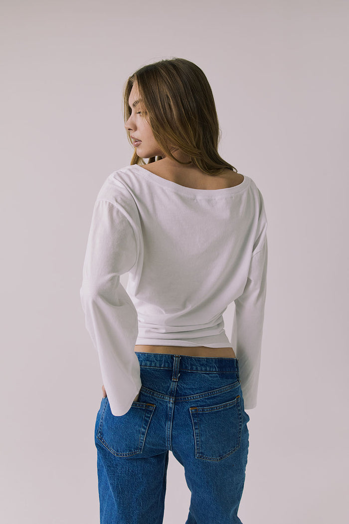 Back view of a woman wearing Chaser's Ash White Long Sleeve and blue jeans against a plain background