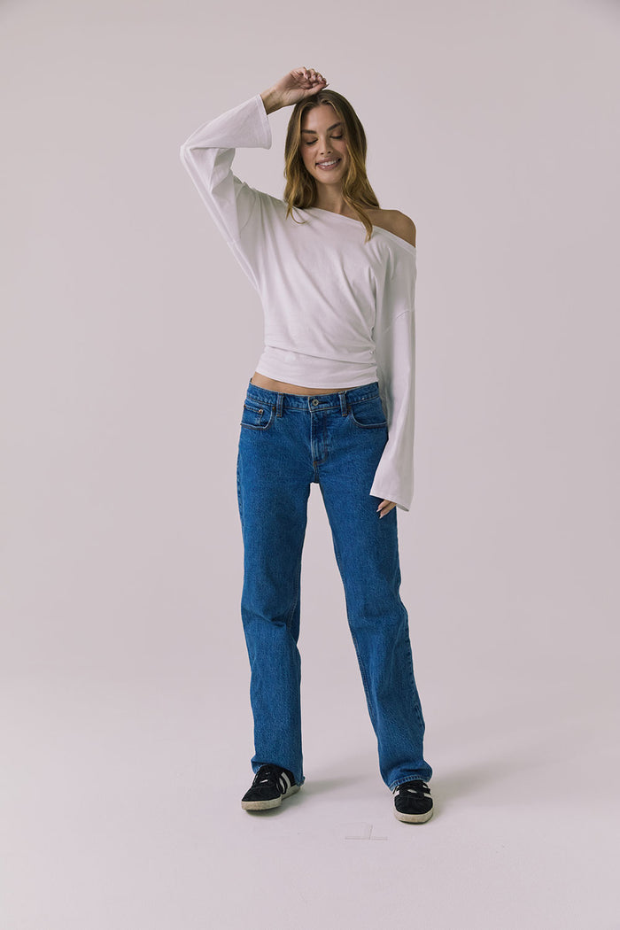 Full body view of a woman wearing Chaser's Ash White Long Sleeve and blue jeans against a plain background