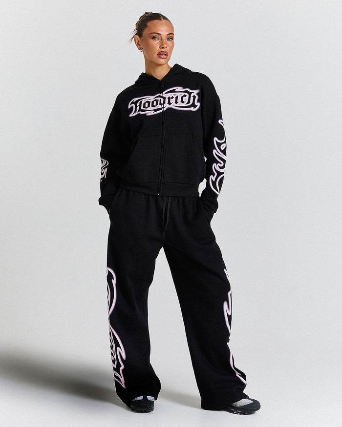Person wearing a black hoodie and pants with white branding on a light gray background