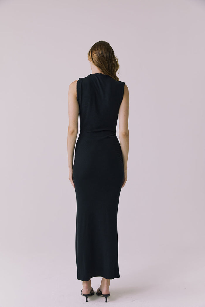 Full body back view of a woman wearing Chaser's Avenue Black Maxi Dress with a slit on a plain background
