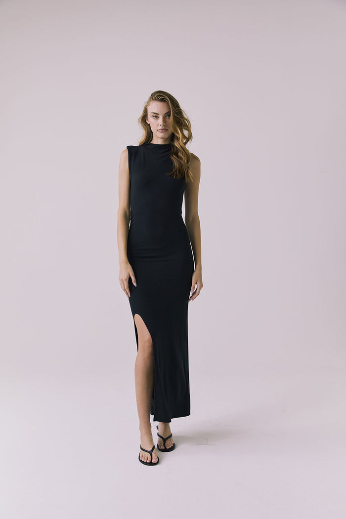 Front view of a woman wearing Chaser's Avenue Black Maxi Dress with a slit on a plain background