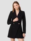 A woman wearing a black blazer mini length with padded shoulders, long sleeves, notched lapel collar, double breasted fastening and a asymmetric pleated skirt panel.