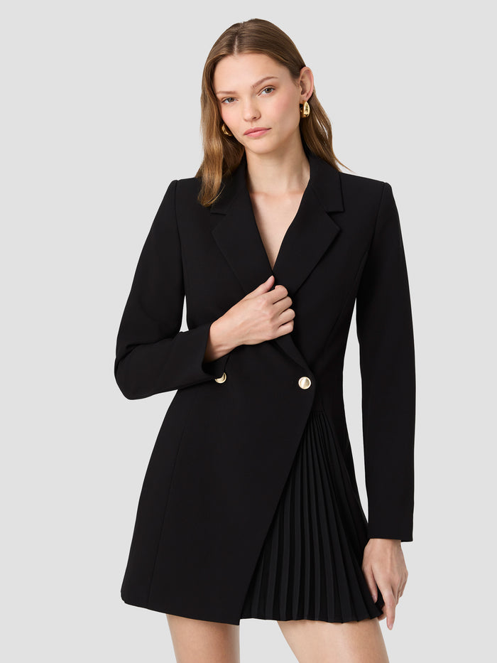 A woman wearing a black blazer mini length with padded shoulders, long sleeves, notched lapel collar, double breasted fastening and a asymmetric pleated skirt panel.