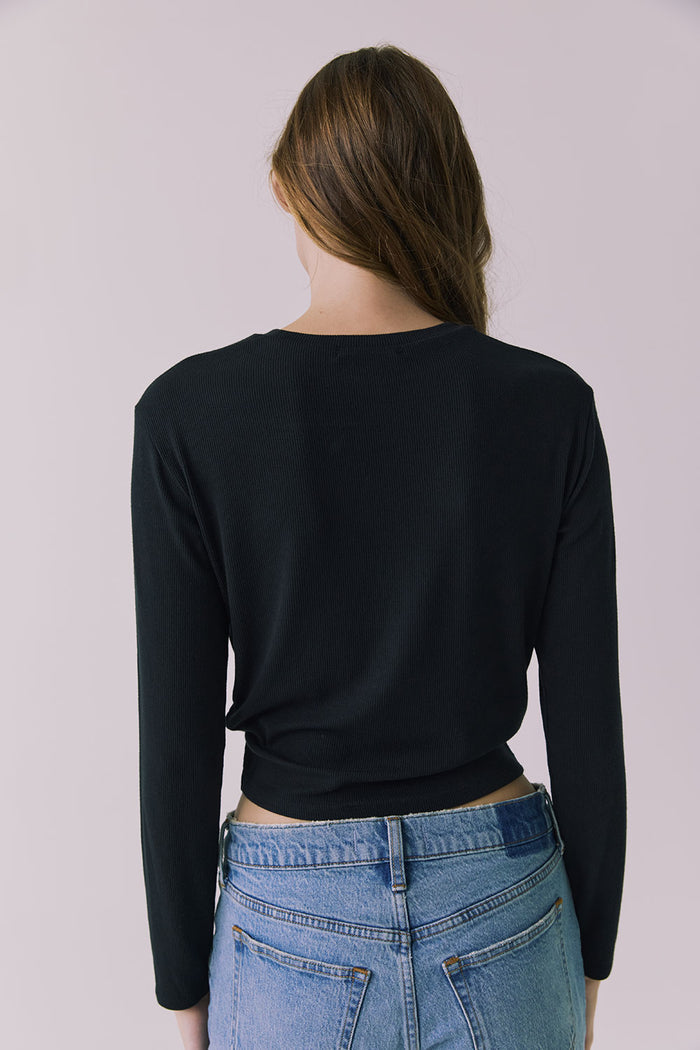Back view of a woman wearing Chaser's Azur Black Long Sleeve top and blue jeans against a plain background