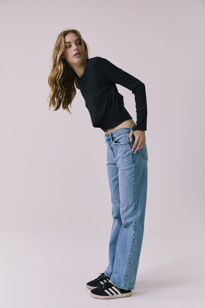 Full body side view of a woman wearing Chaser's Azur Black Long Sleeve top and blue jeans against a plain background