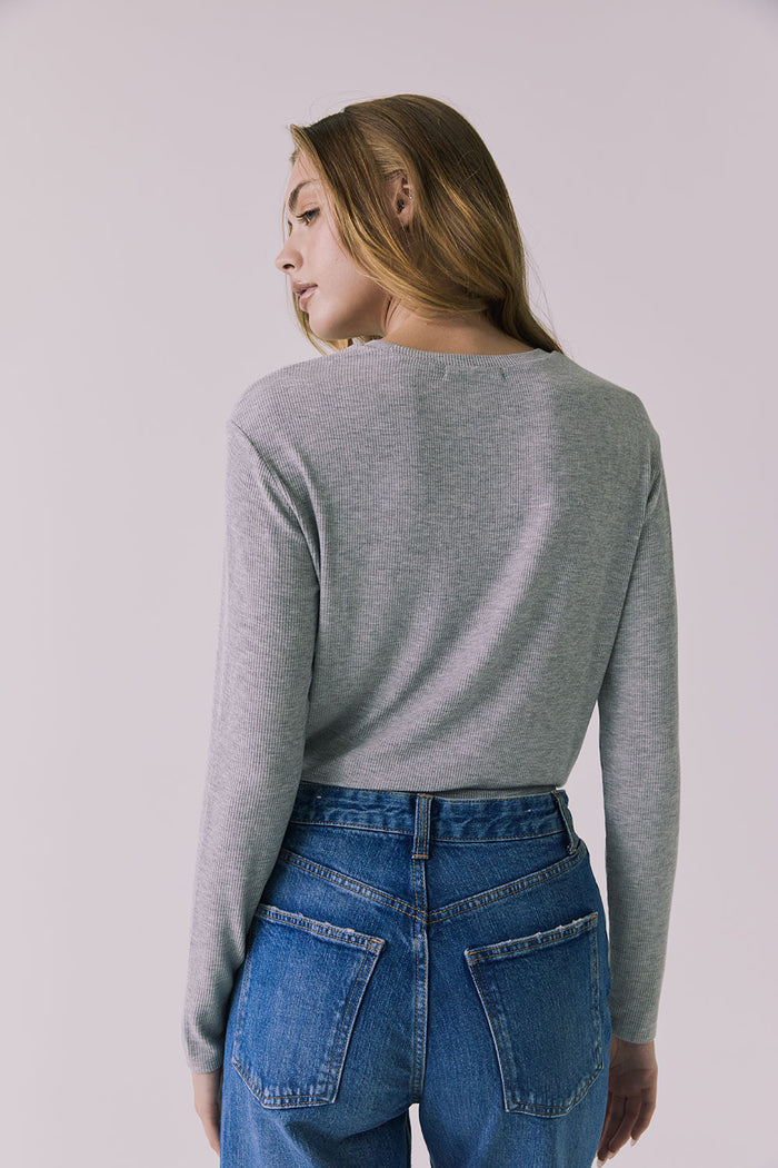 Back view of a woman wearing Chaser's Azur Heather Grey Long Sleeve top and blue jeans against a plain background