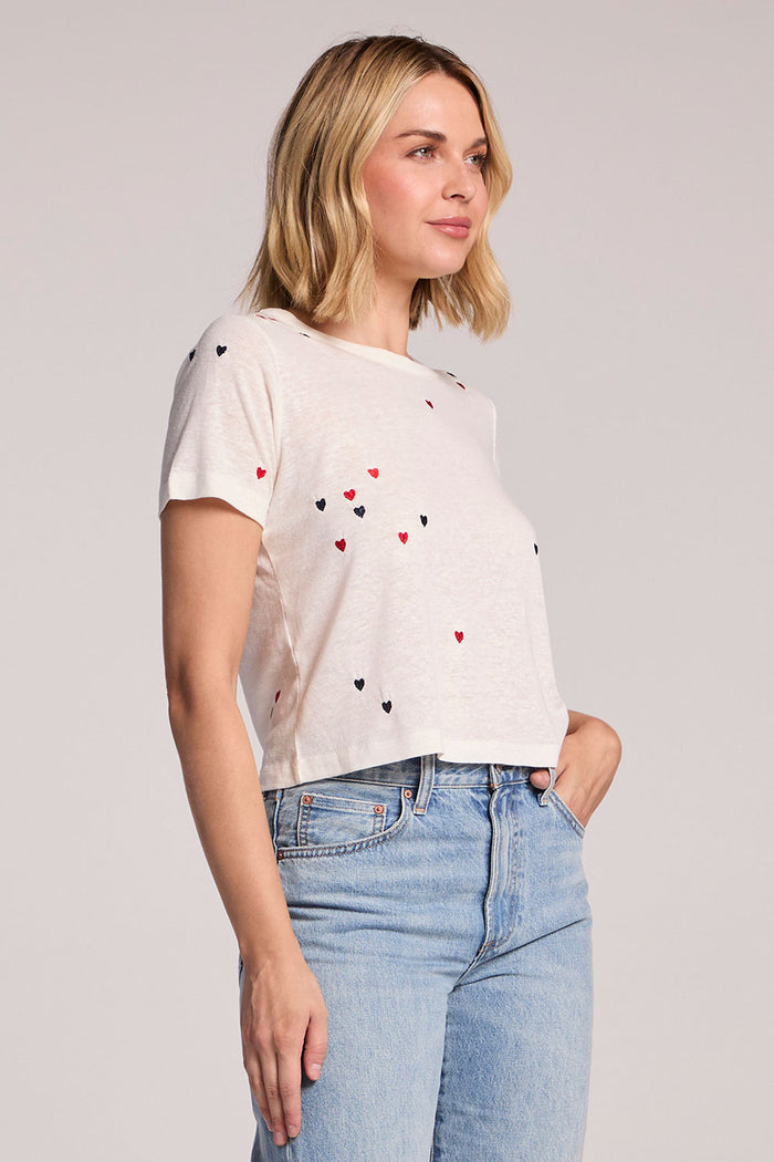 Side view of a woman wearing the Chaser Baby Heart Toss Tee on a neutral background with one hand in her pocket