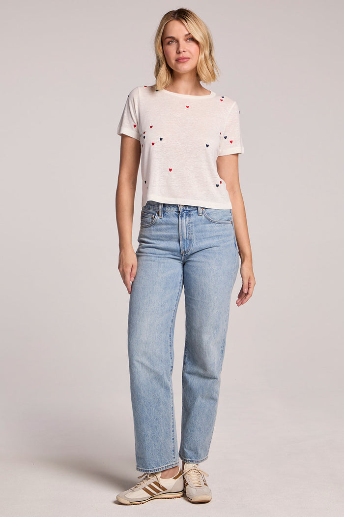 Front view of a woman wearing the Chaser Baby Heart Toss Tee and sneakers on a neutral background
