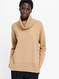 A woman wearing a beige jumper with a cowl neck, long sleeves and a relaxed fit.