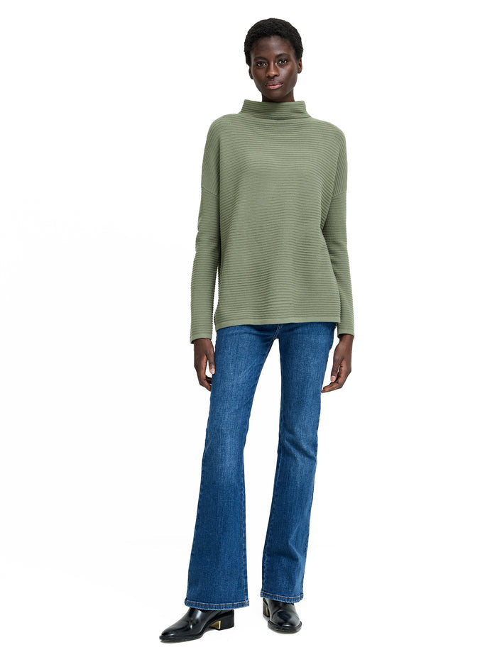 A woman wearing a khaki knit Jumper with long sleeves, a high neckline and a relaxed fit.