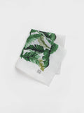 White linen pocket square with a green banana leaf print, folded.