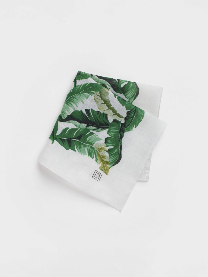 White linen pocket square with a green banana leaf print, folded.