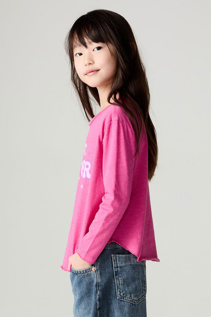 Side view of a girl wearing the Chaser Best Sister Girls Tee on a neutral background and blue jeans