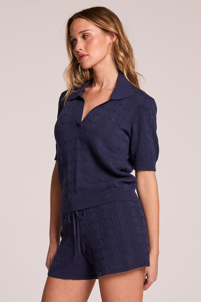 Side angle view of a woman wearing the Chaser  Bijou Admiral Polo  on a neutral background with arms at her sides