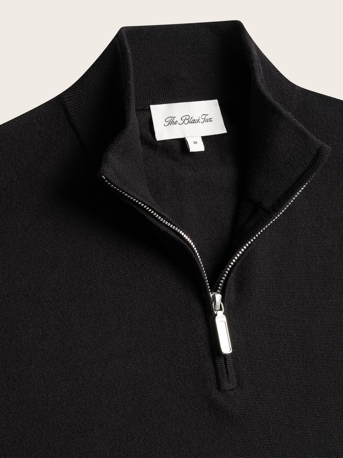 Close-up of a black quarter-zip sweater's collar and zipper pull with brand tag.
