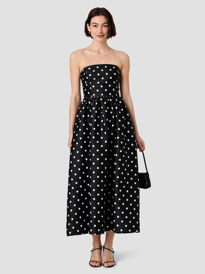 A woman wearing a black and white bandeau midi length  taffeta Dress with a polka dot pattern, removable adjustable straps, a invisible back zip fastening and a structured skirt.