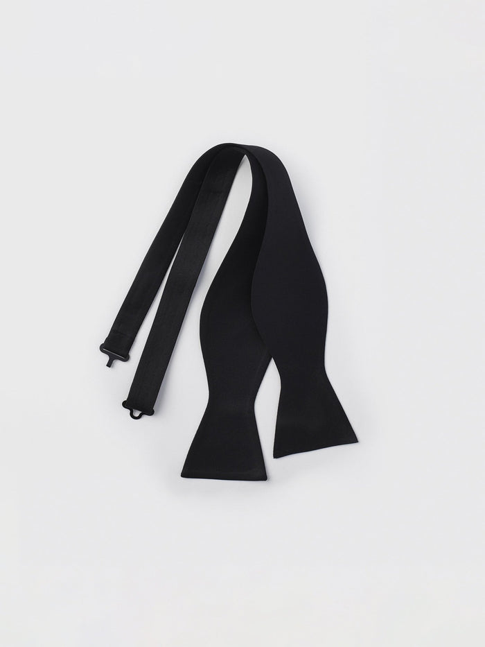 Untied black bow tie laid flat on a white background.