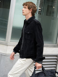 A man wearing a corduroy black Jacket with long sleeves, a point collar, 2 chested pockets, and a snap button fastening.